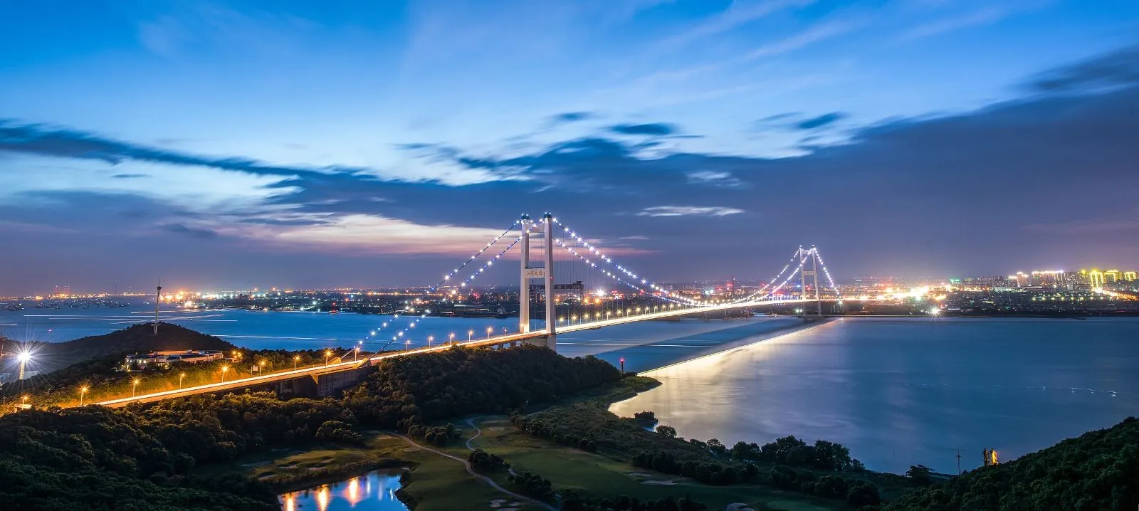 The illuminated Yangtze River bridge at Jiangyin seen across the water at dusk