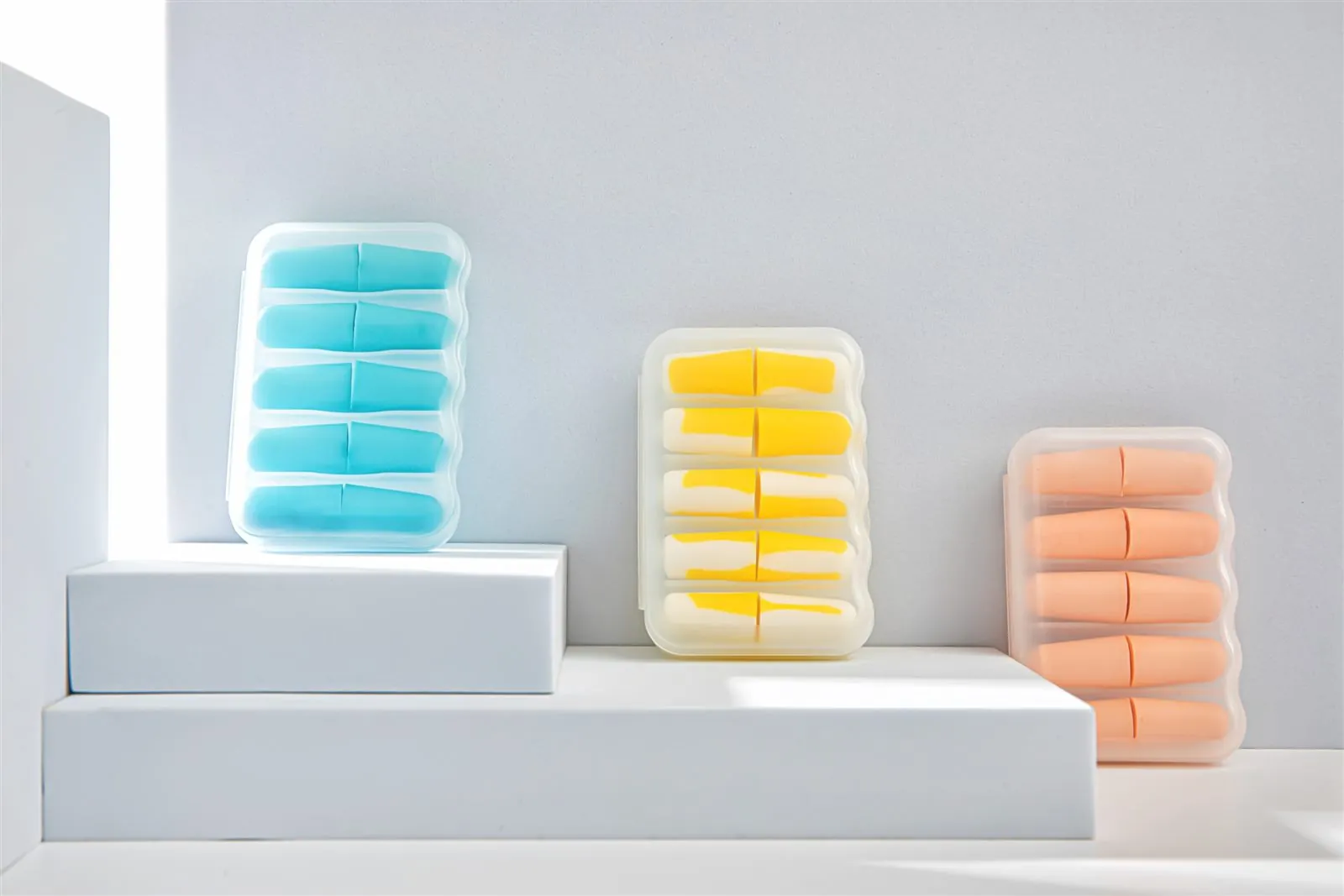 Foam earplugs in colour-matched travel cases on white display blocks